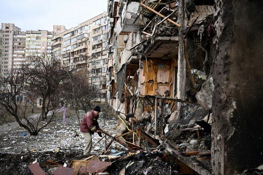 A man clears debris at a damaged residential building at Koshytsa Street, a suburb of the Ukrainian capital Kyiv, where a military shell allegedly hit, on February 25, 2022. - Russian forces reached the outskirts of Kyiv on Friday as Ukrainian President Volodymyr Zelensky said the invading troops were targeting civilians and explosions could be heard in the besieged capital. Pre-dawn blasts in Kyiv set off a second day of violence after Russian President Vladimir Putin defied Western warnings to unleash a full-scale ground invasion and air assault on Thursday that quickly claimed dozens of lives and displaced at least 100,000 people. (Photo by Daniel LEAL / AFP)